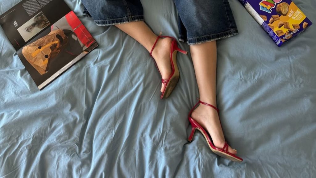Mujer usando sandalias kitten heels en Chile, acostada en cama con libros al rededor. Imagen del Instagram @genemacazana. Permiso de uso entregado por la influencer.