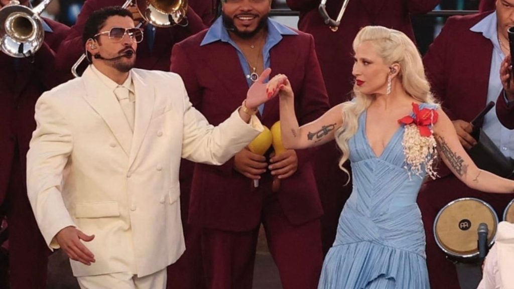 Bad Bunny y Lady Gaga tomados de la mano durante el show de medio tiempo del Super Bowl, con músicos al fondo y vestuario de LUAR