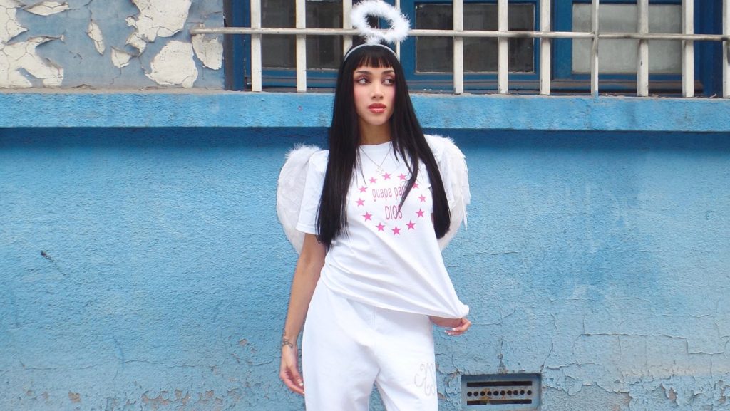 Modelo con un total look en blanco. Lleva una polera con mangas corta con la leyenda "guapa para Dios". Es parte del look 2 de la nueva cápsula de KANDELABRO