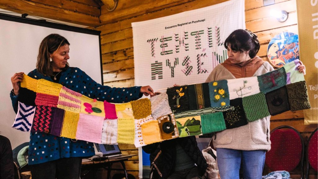 Dos artesanas sujetan un telar hecho a mano. Atrás se ve un cartel que dice Textil Aysén. La imagen es parte de la presentación de la segunda edición del evento. ph: Pulso Austral
