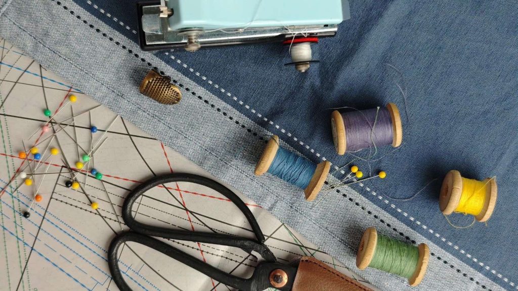 Mesa con telas, hilos, agujas, representando la economía circular y arreglos de ropa. EN representación de Fundación textil Circular. Imagen libre de uso.